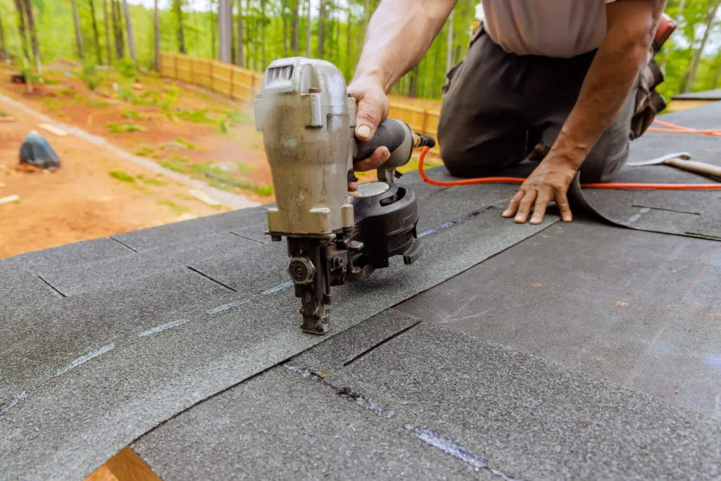Roofer nailing new shingles with a pneumatic nail gun